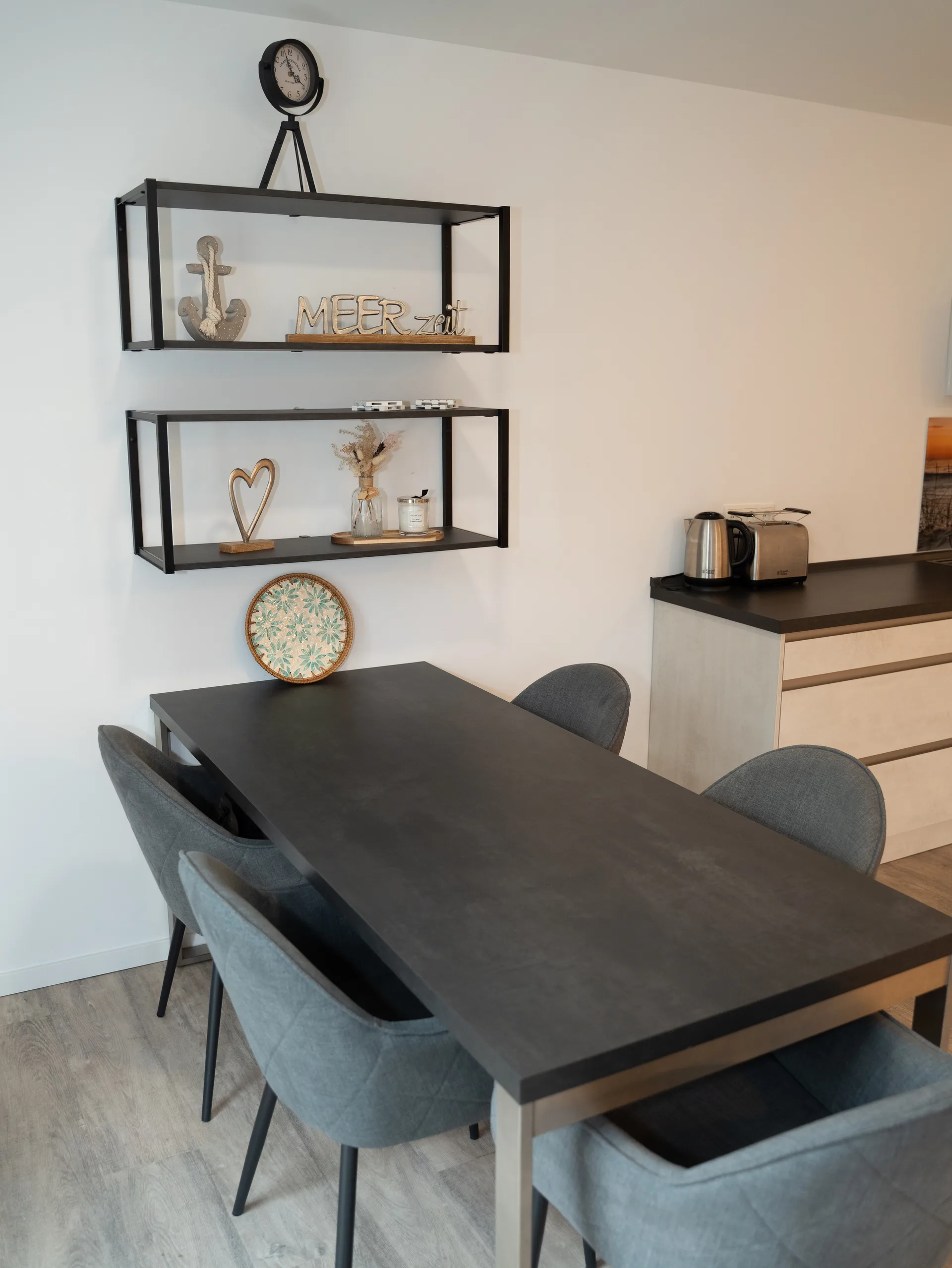 Essbereich mit Esstisch für fünf Personen und maritimen Wandregalen in der Kurparkperle Grömitz