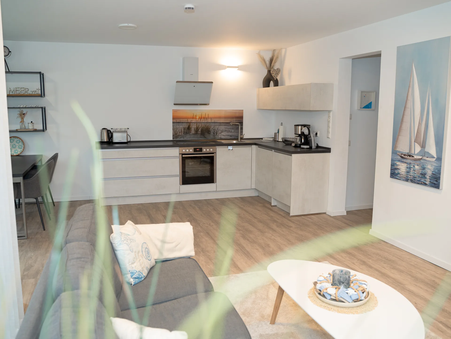 Blick durch eine Grünpflanze auf den offenen Wohn- und Küchenbereich der Kurparkperle